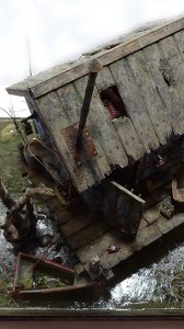 Diorama artístico de una cabaña de madera azul envejecida sobre pilotes en un pantano, con efectos de agua estancada, un bote de remos y detalles de vegetación pantanosa.