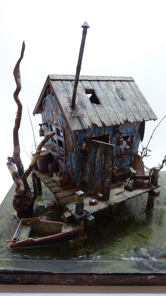 Miniatura de cabaña pantanosa con estructura desmontable. Diorama de realismo extremo con texturas de madera podrida, vegetación de ciénaga y agua de resina. Obra de modelismo artesanal con interior totalmente decorado por 27dioramas.