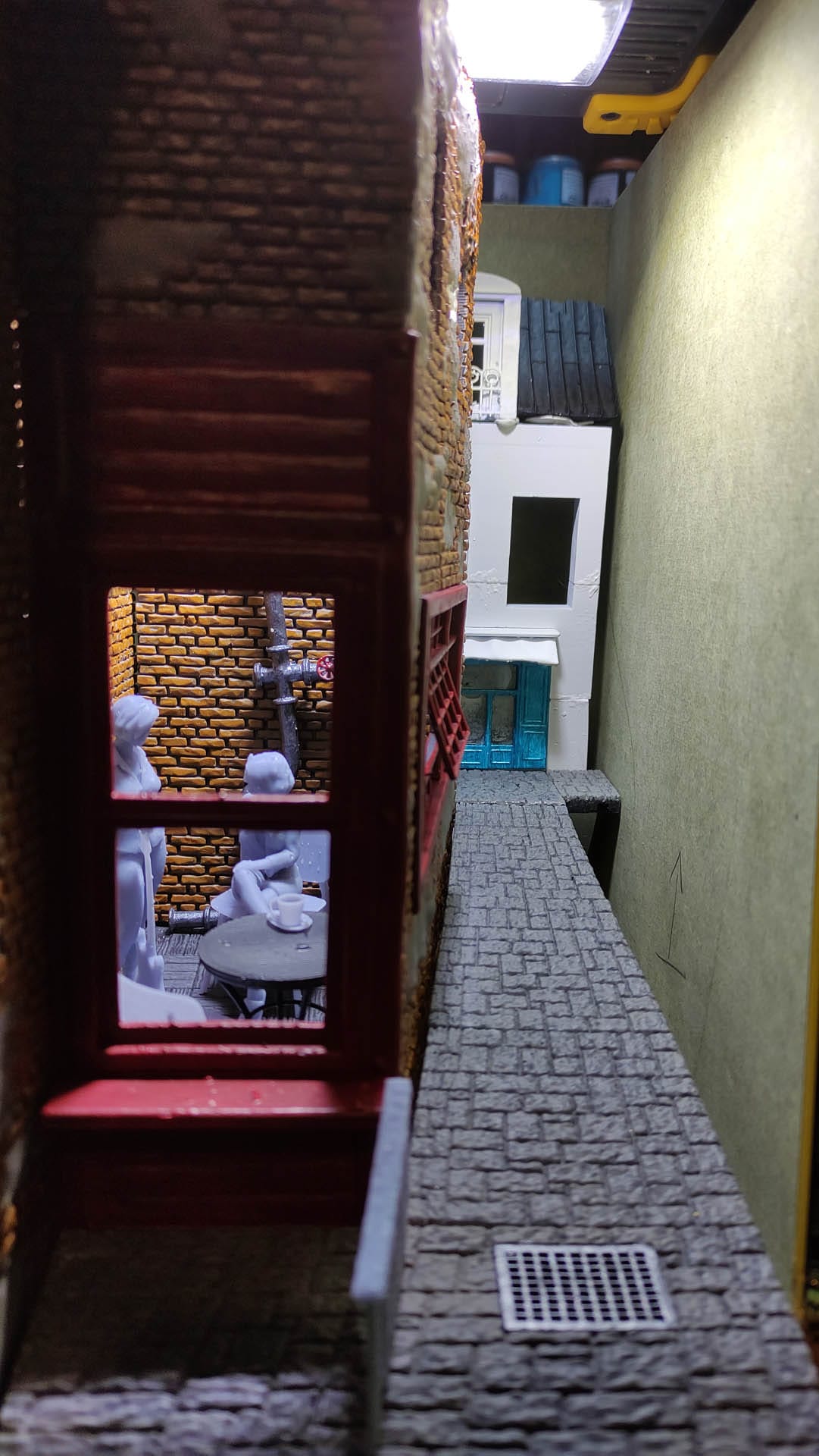 Diorama de una calle de París con fachadas de ladrillo, iluminación LED cálida y perspectiva forzada.