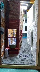 Diorama de una calle de París con fachadas de ladrillo, iluminación LED cálida y perspectiva forzada.