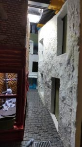 Diorama de una calle de París con fachadas de ladrillo, iluminación LED cálida y perspectiva forzada.