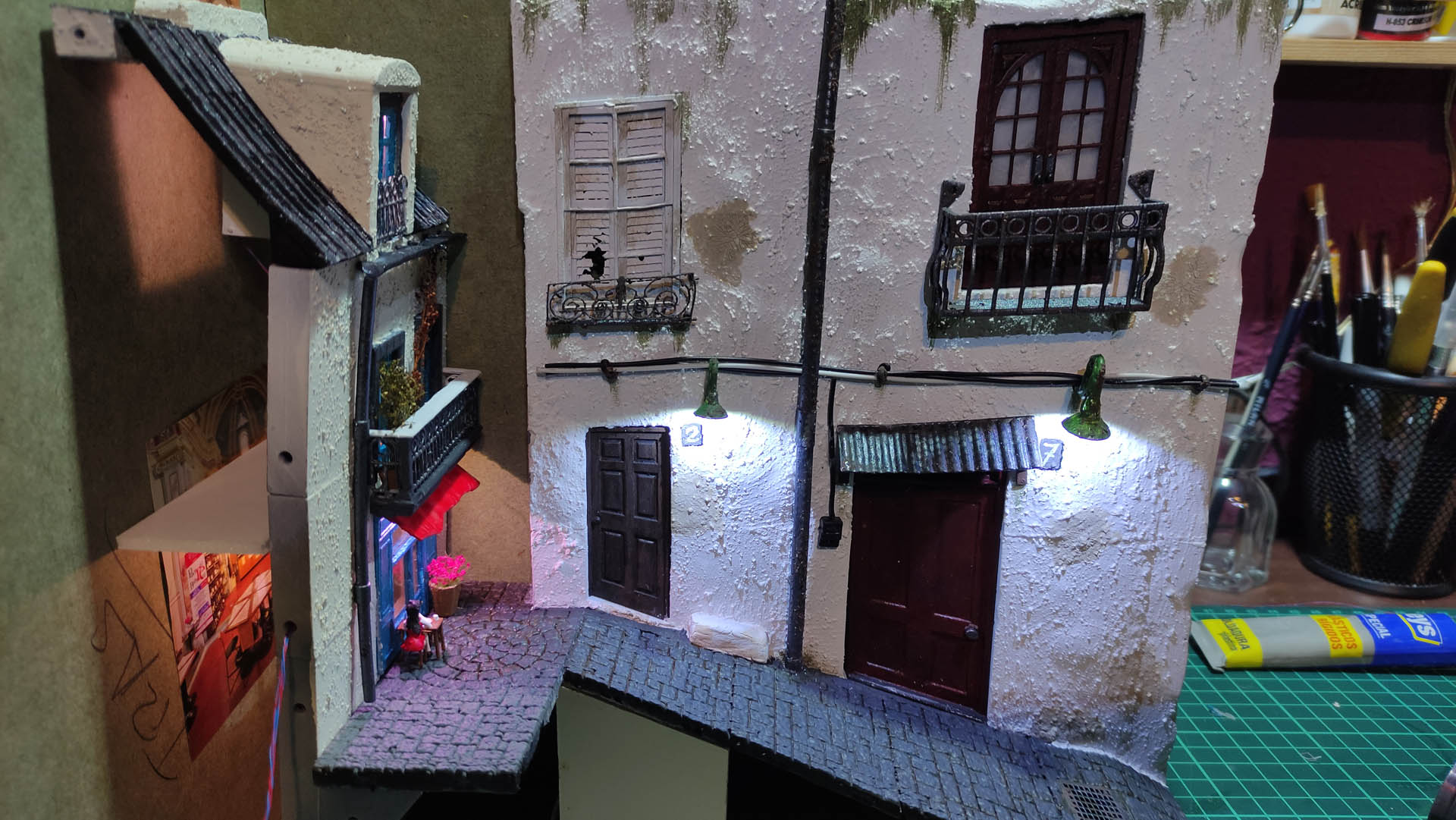 Diorama de una calle de París con fachadas de ladrillo, iluminación LED cálida y perspectiva forzada.