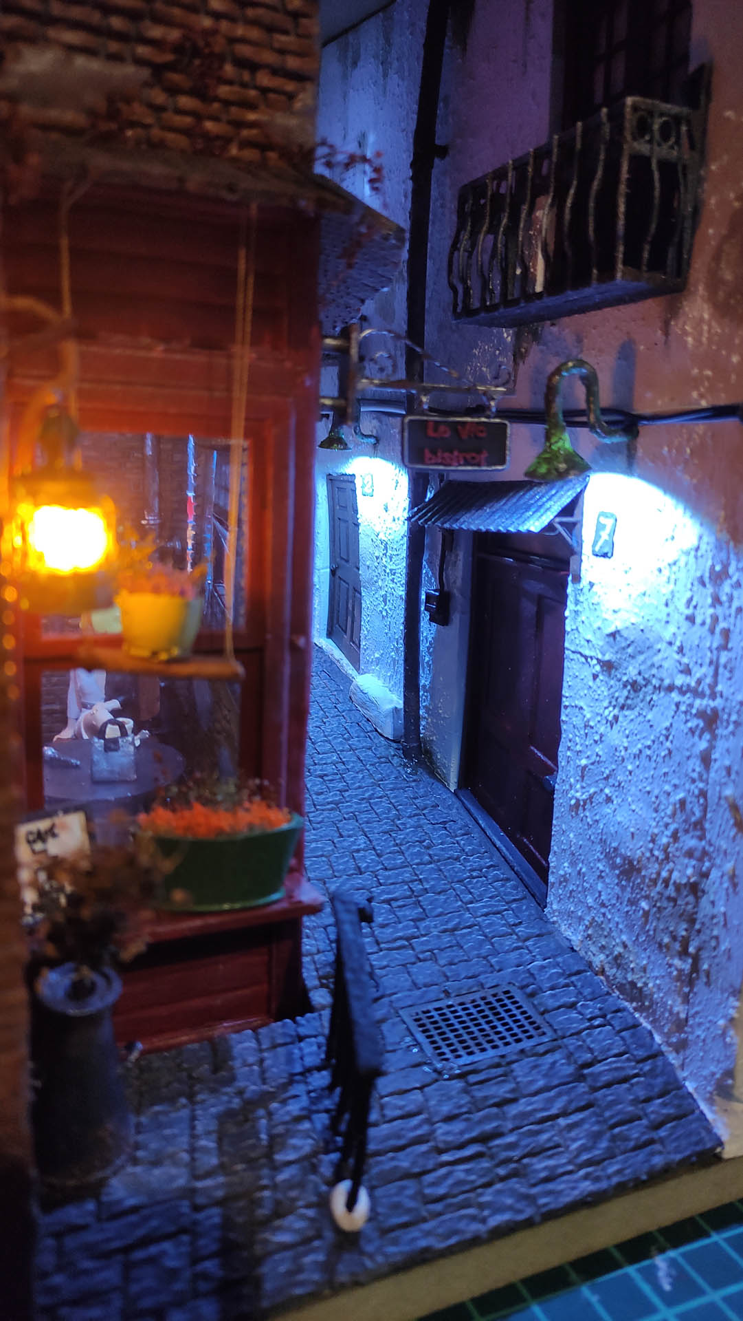 Diorama de una calle de París con fachadas de ladrillo, iluminación LED cálida y perspectiva forzada.