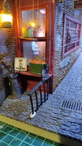 Diorama de una calle de París con fachadas de ladrillo, iluminación LED cálida y perspectiva forzada.