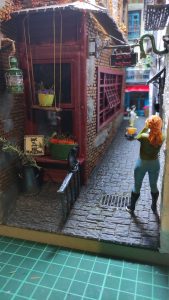 Diorama de una calle de París con fachadas de ladrillo, iluminación LED cálida y perspectiva forzada.