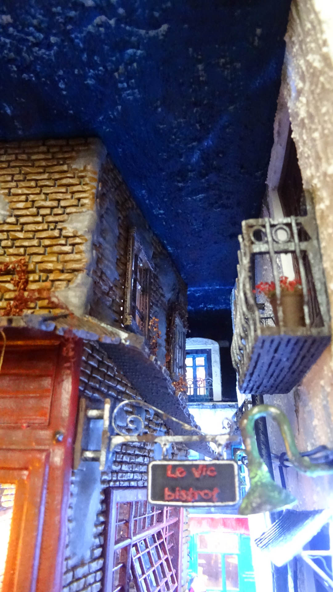 Diorama de una calle de París con fachadas de ladrillo, iluminación LED cálida y perspectiva forzada.