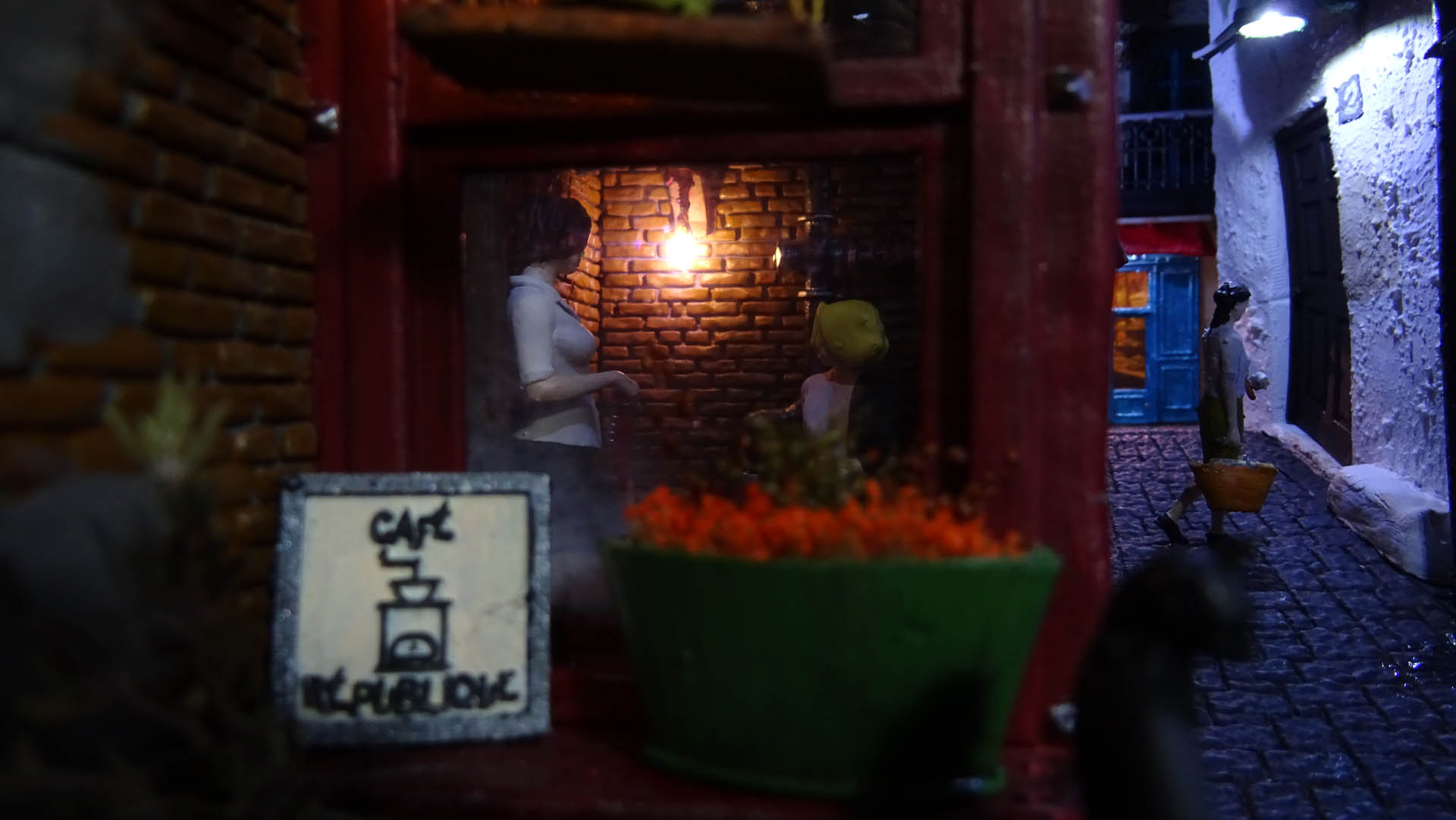 Diorama de una calle de París con fachadas de ladrillo, iluminación LED cálida y perspectiva forzada.