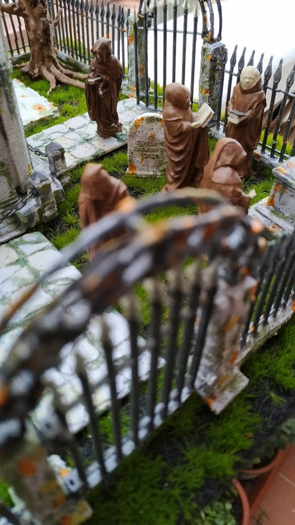 Diorama de un cementerio gótico artesanal con mausoleo central, monjes encapuchados y detalles de vegetación realista.