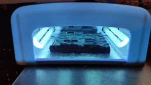 Proceso de curado de piezas de resina UV bajo luz ultravioleta en el taller