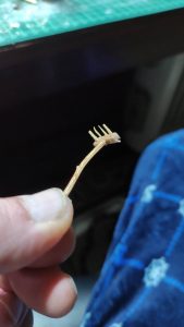 Mano sosteniendo una pequeña rama en miniatura con forma de rastrillo o horca, elaborada artesanalmente con palitos de madera, para uso en diorama