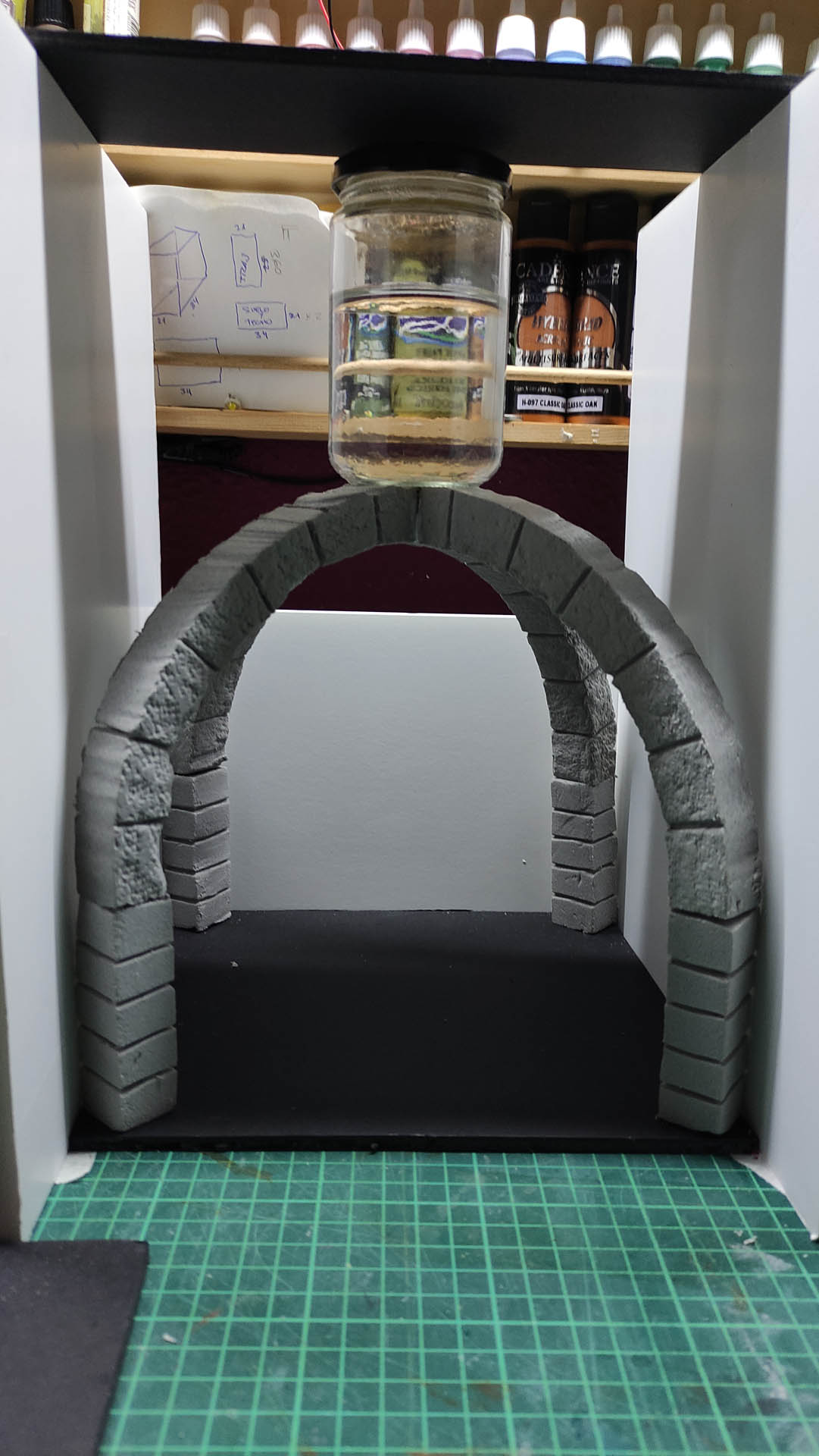 Arco de piedra en miniatura texturizado y pintado en gris, con sillares tallados uno a uno, colocado dentro de la estructura de un diorama en construcción