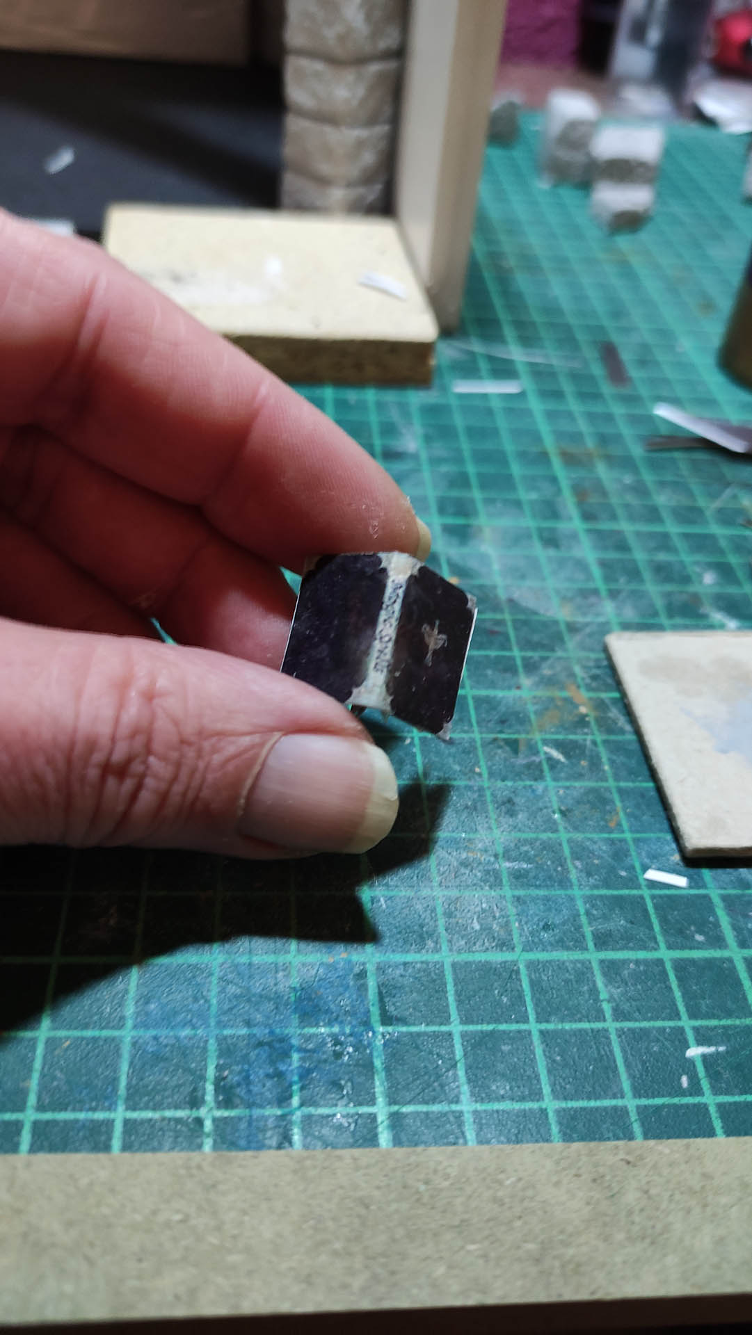 Libro en miniatura hecho a mano, con cubierta en tono negro y detalles pintados a mano, sostenido entre los dedos para mostrar su pequeño tamaño en comparación con la mano humana