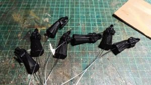 Figuras en miniatura de la Santa Compaña en proceso de elaboración, representando las figuras encapuchadas de la procesión de ánimas, junto a piezas ovaladas translúcidas que simularán los cirios, y un rollo de hilo de fibra óptica para la iluminación de las velas del diorama