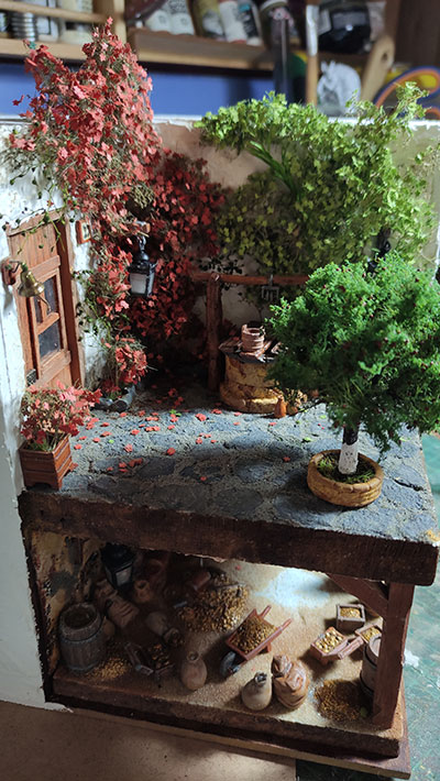 Miniatura de leyenda cordobesa hecha con corcho extruido, yeso y arcilla polimérica. Diorama detallado de un patio andaluz con pozo y un nivel inferior que muestra un tesoro escondido custodiado por un duende, obra artesanal de 27dioramas.