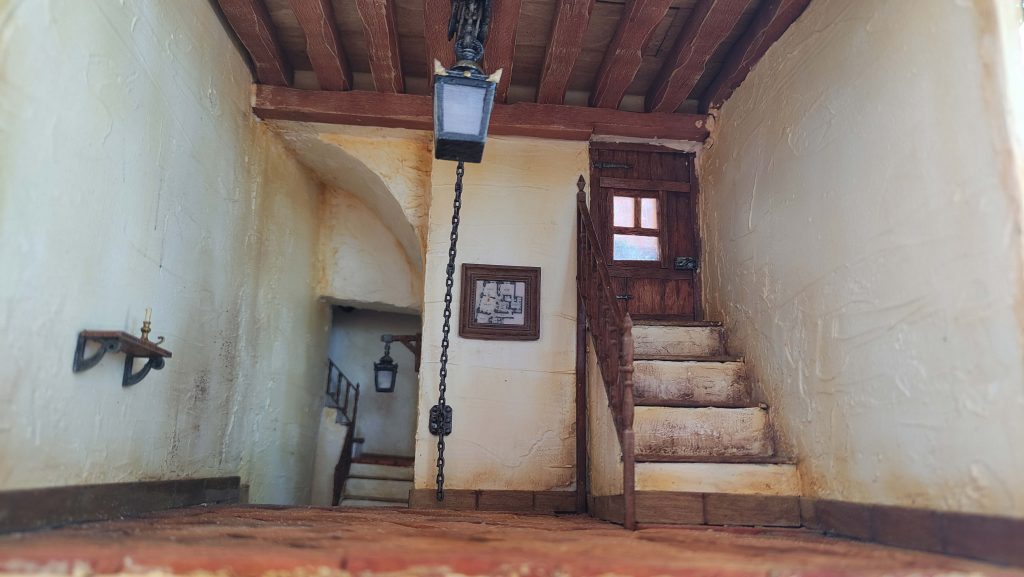 Diorama de portal cordobés con suelo de barro cocido, escaleras a viviendas y acceso secreto al sótano del duende