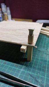 Diorama artístico de una cabaña de madera azul envejecida sobre pilotes en un pantano, con efectos de agua estancada, un bote de remos y detalles de vegetación pantanosa.