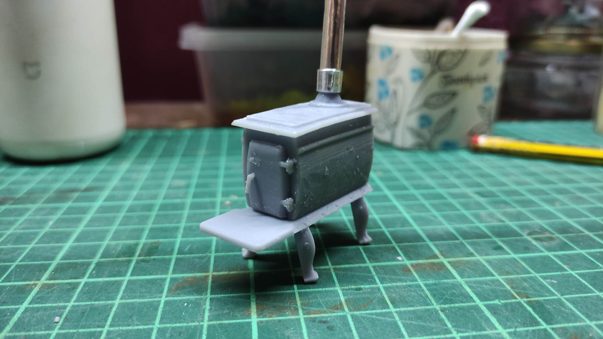 Diorama artístico de una cabaña de madera azul envejecida sobre pilotes en un pantano, con efectos de agua estancada, un bote de remos y detalles de vegetación pantanosa.