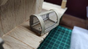 Diorama artístico de una cabaña de madera azul envejecida sobre pilotes en un pantano, con efectos de agua estancada, un bote de remos y detalles de vegetación pantanosa.