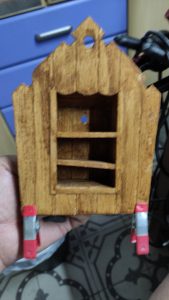 Diorama artístico de una cabaña de madera azul envejecida sobre pilotes en un pantano, con efectos de agua estancada, un bote de remos y detalles de vegetación pantanosa.