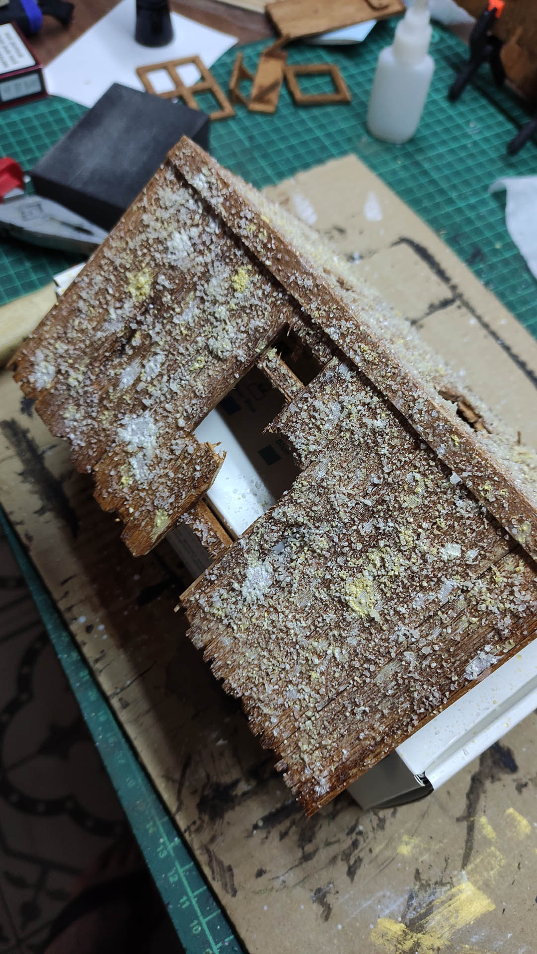 Diorama artístico de una cabaña de madera azul envejecida sobre pilotes en un pantano, con efectos de agua estancada, un bote de remos y detalles de vegetación pantanosa.