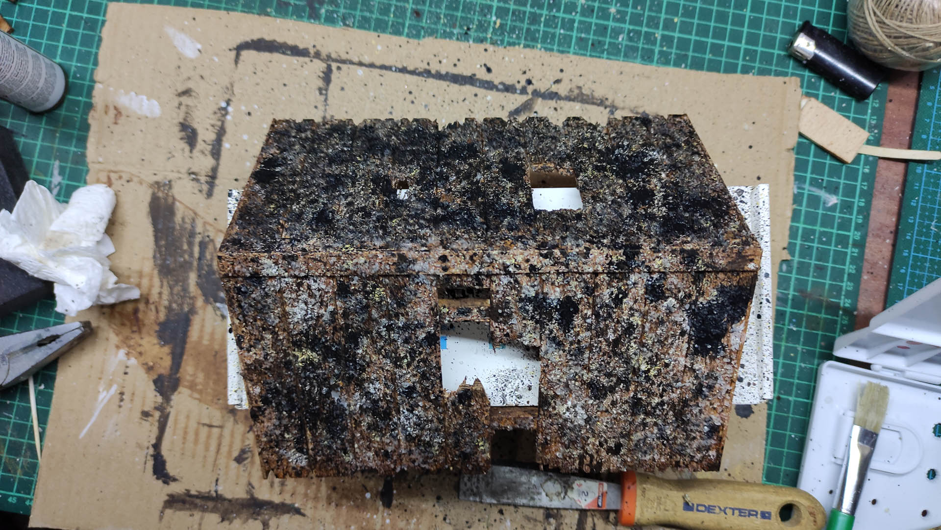 Diorama artístico de una cabaña de madera azul envejecida sobre pilotes en un pantano, con efectos de agua estancada, un bote de remos y detalles de vegetación pantanosa.