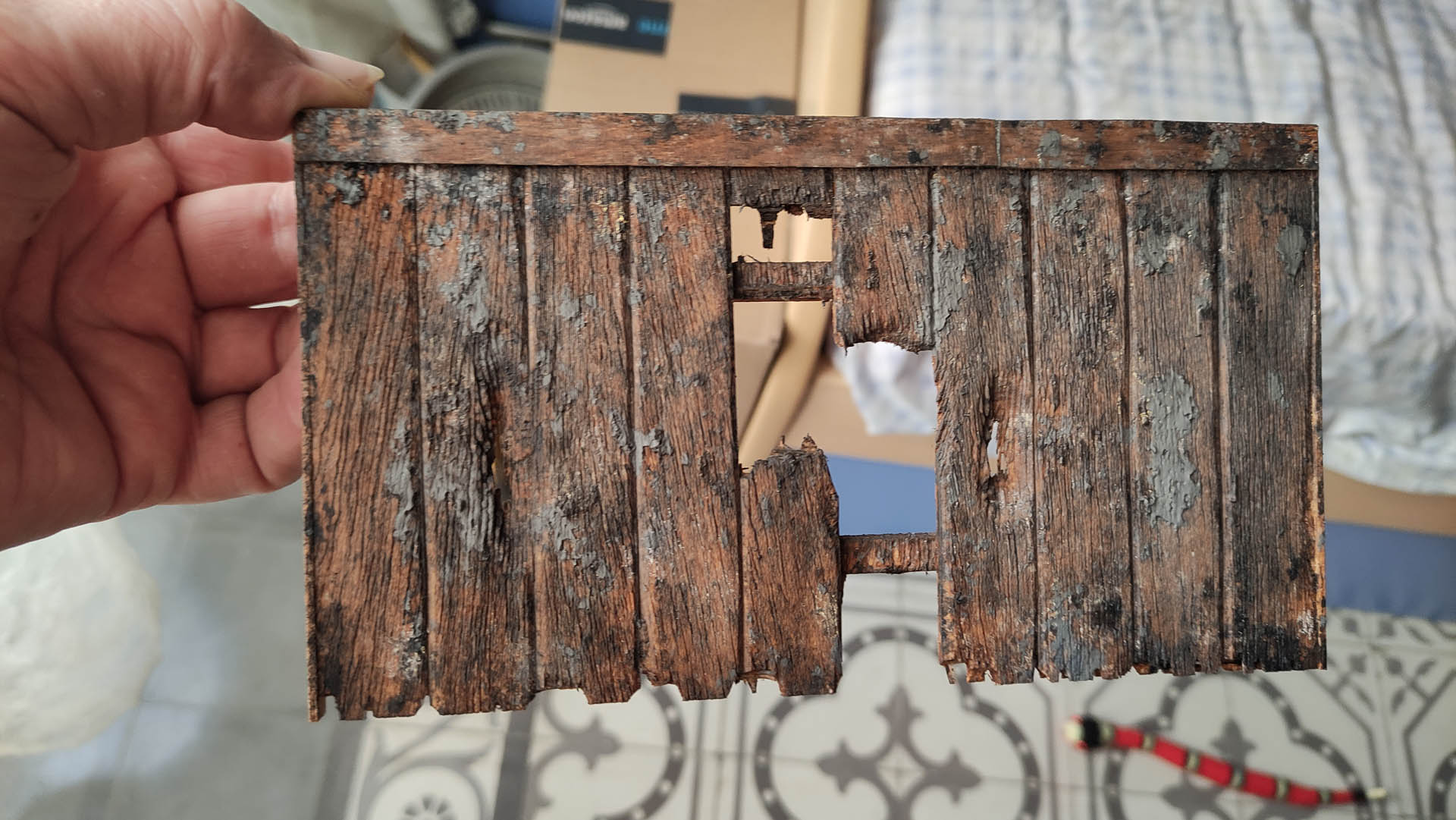 Diorama artístico de una cabaña de madera azul envejecida sobre pilotes en un pantano, con efectos de agua estancada, un bote de remos y detalles de vegetación pantanosa.