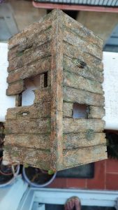 Diorama artístico de una cabaña de madera azul envejecida sobre pilotes en un pantano, con efectos de agua estancada, un bote de remos y detalles de vegetación pantanosa.