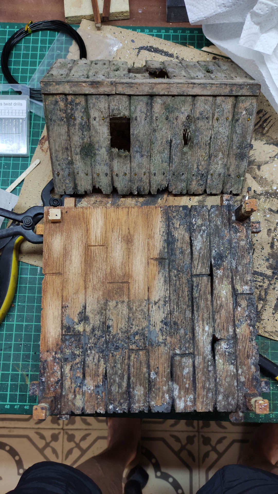 Diorama artístico de una cabaña de madera azul envejecida sobre pilotes en un pantano, con efectos de agua estancada, un bote de remos y detalles de vegetación pantanosa.