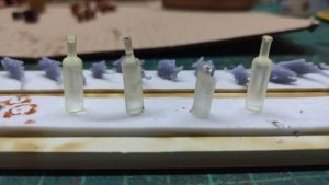 Diorama artístico de una cabaña de madera azul envejecida sobre pilotes en un pantano, con efectos de agua estancada, un bote de remos y detalles de vegetación pantanosa.