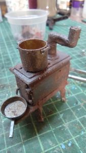 Diorama artístico de una cabaña de madera azul envejecida sobre pilotes en un pantano, con efectos de agua estancada, un bote de remos y detalles de vegetación pantanosa.