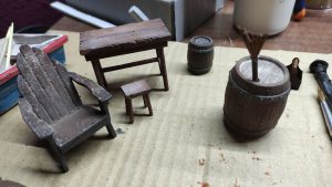 Diorama artístico de una cabaña de madera azul envejecida sobre pilotes en un pantano, con efectos de agua estancada, un bote de remos y detalles de vegetación pantanosa.