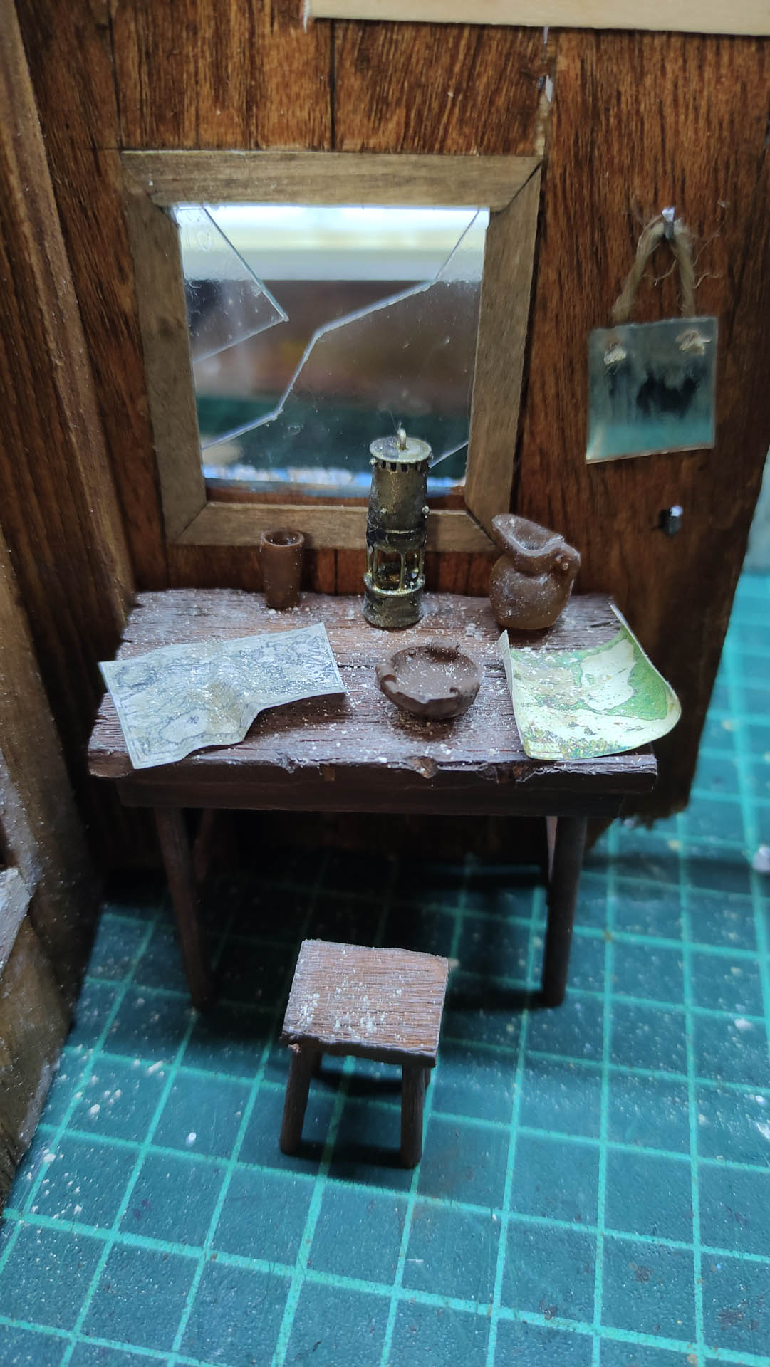 Diorama artístico de una cabaña de madera azul envejecida sobre pilotes en un pantano, con efectos de agua estancada, un bote de remos y detalles de vegetación pantanosa.