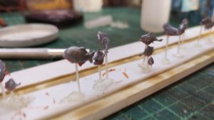 Diorama artístico de una cabaña de madera azul envejecida sobre pilotes en un pantano, con efectos de agua estancada, un bote de remos y detalles de vegetación pantanosa.