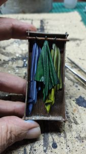 Diorama artístico de una cabaña de madera azul envejecida sobre pilotes en un pantano, con efectos de agua estancada, un bote de remos y detalles de vegetación pantanosa.