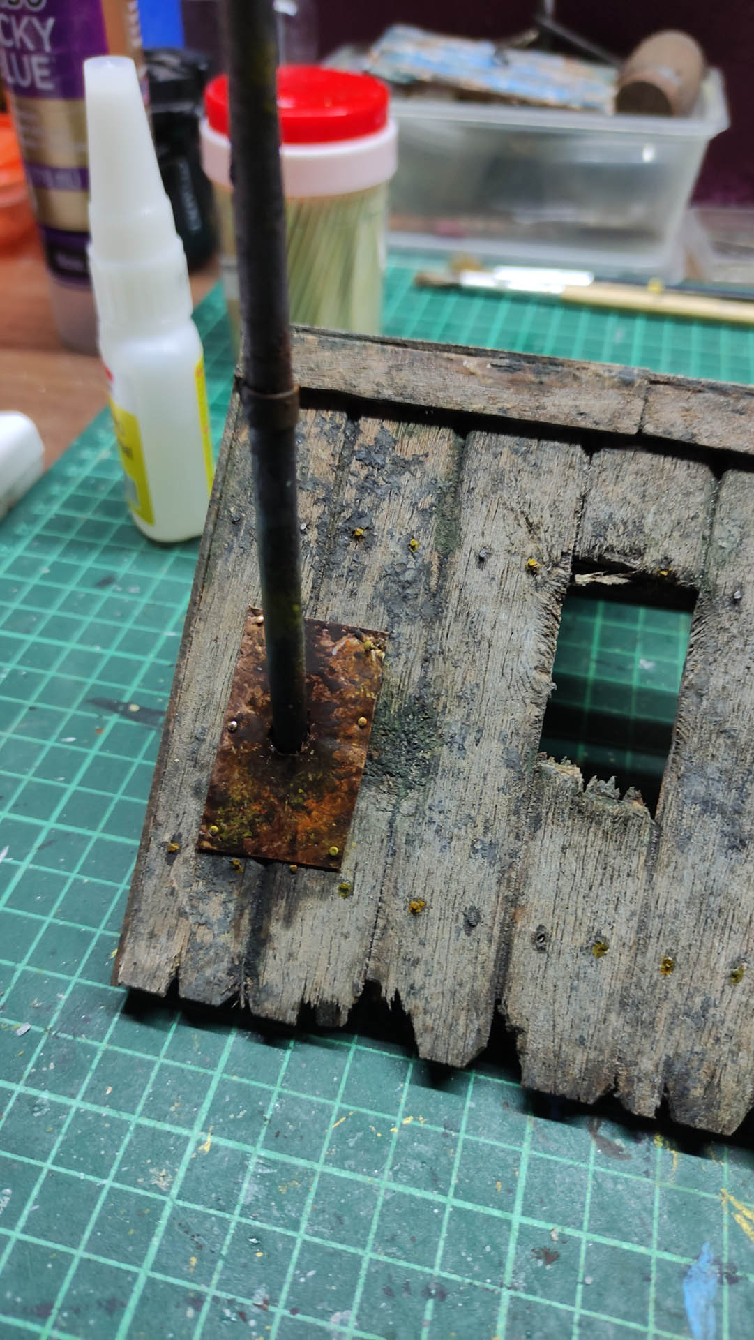 Diorama artístico de una cabaña de madera azul envejecida sobre pilotes en un pantano, con efectos de agua estancada, un bote de remos y detalles de vegetación pantanosa.