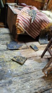 Diorama artístico de una cabaña de madera azul envejecida sobre pilotes en un pantano, con efectos de agua estancada, un bote de remos y detalles de vegetación pantanosa.