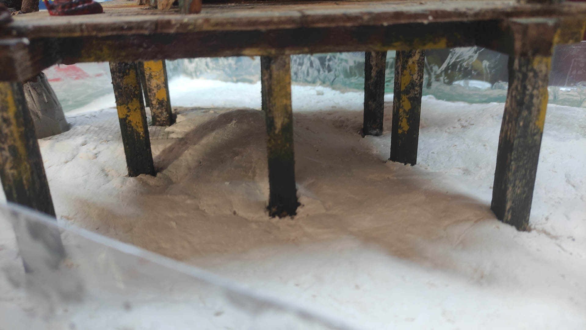 Diorama artístico de una cabaña de madera azul envejecida sobre pilotes en un pantano, con efectos de agua estancada, un bote de remos y detalles de vegetación pantanosa.