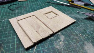 Diorama artístico de una cabaña de madera azul envejecida sobre pilotes en un pantano, con efectos de agua estancada, un bote de remos y detalles de vegetación pantanosa.