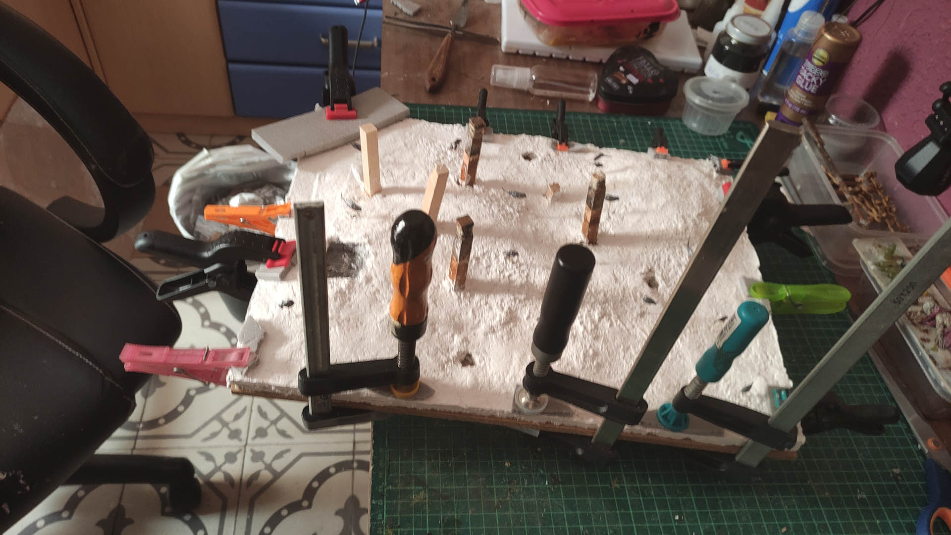 Diorama artístico de una cabaña de madera azul envejecida sobre pilotes en un pantano, con efectos de agua estancada, un bote de remos y detalles de vegetación pantanosa.