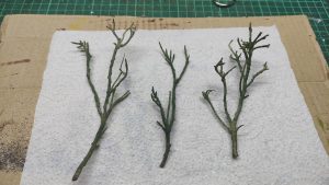 Diorama artístico de una cabaña de madera azul envejecida sobre pilotes en un pantano, con efectos de agua estancada, un bote de remos y detalles de vegetación pantanosa.