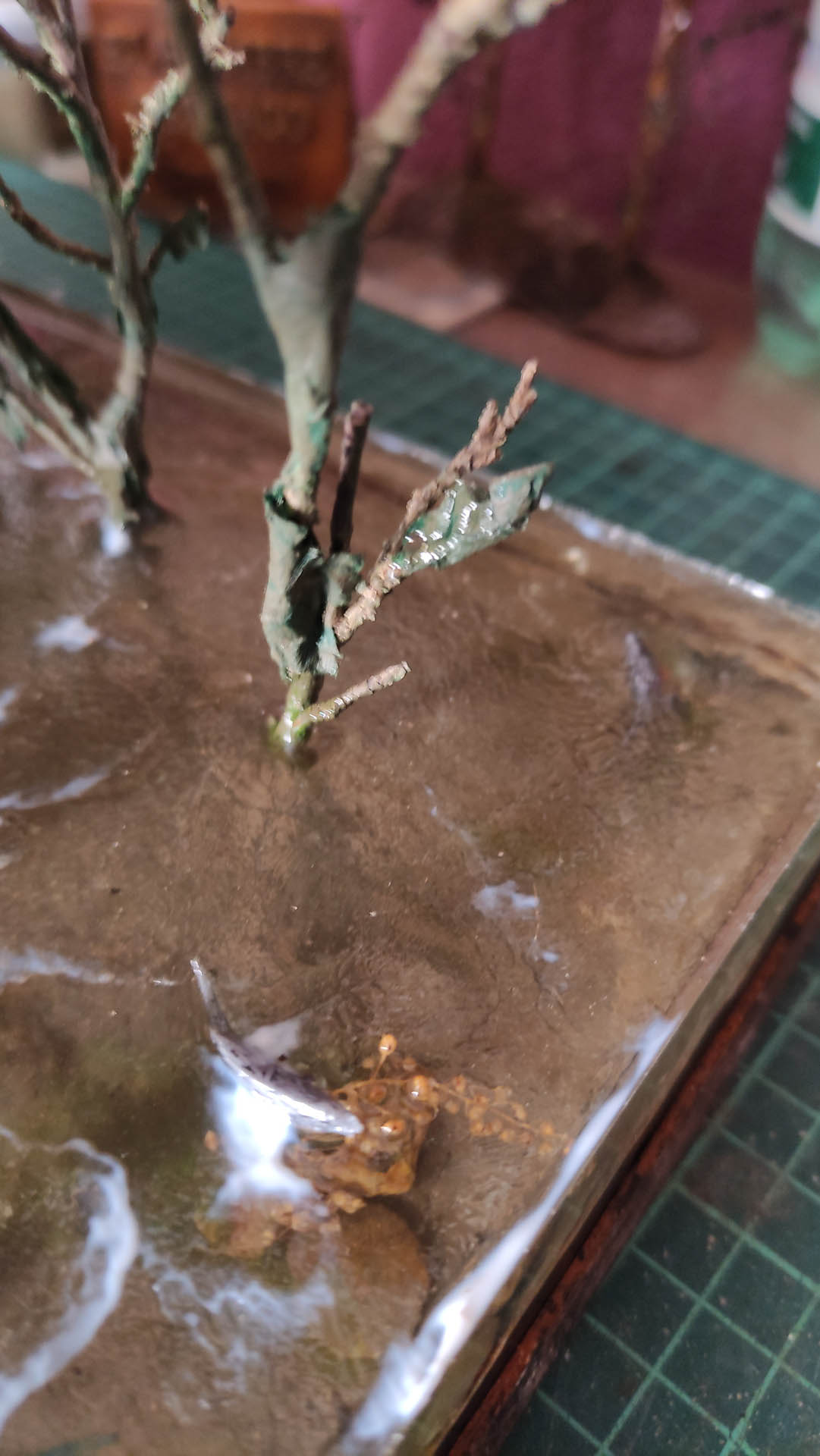 Diorama artístico de una cabaña de madera azul envejecida sobre pilotes en un pantano, con efectos de agua estancada, un bote de remos y detalles de vegetación pantanosa.