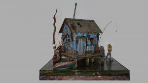 Diorama artístico de una cabaña de madera azul envejecida sobre pilotes en un pantano, con efectos de agua estancada, un bote de remos y detalles de vegetación pantanosa.