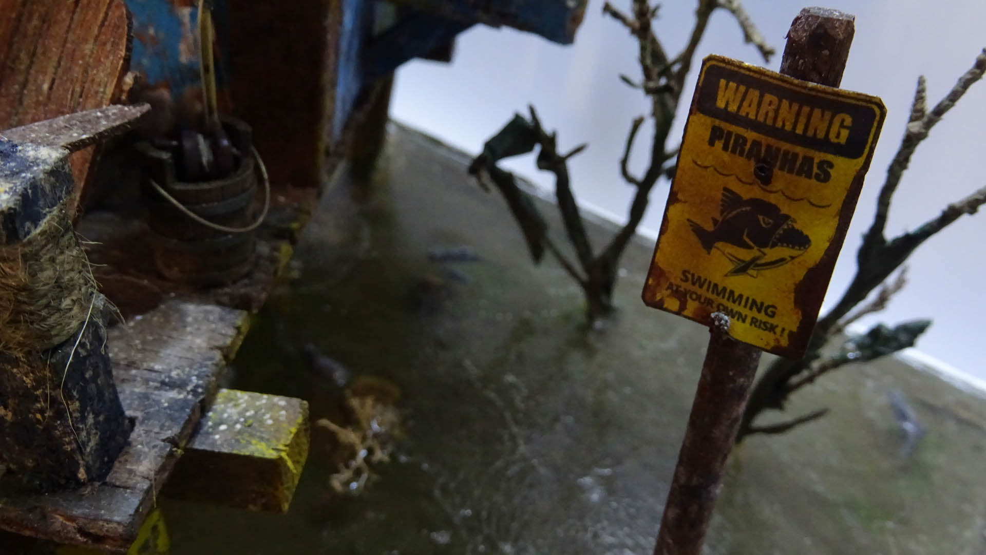 Diorama artístico de una cabaña de madera azul envejecida sobre pilotes en un pantano, con efectos de agua estancada, un bote de remos y detalles de vegetación pantanosa.