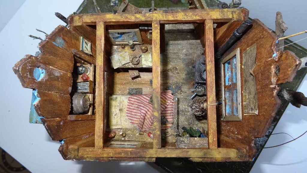 Diorama artístico de una cabaña de madera azul envejecida sobre pilotes en un pantano, con efectos de agua estancada, un bote de remos y detalles de vegetación pantanosa.