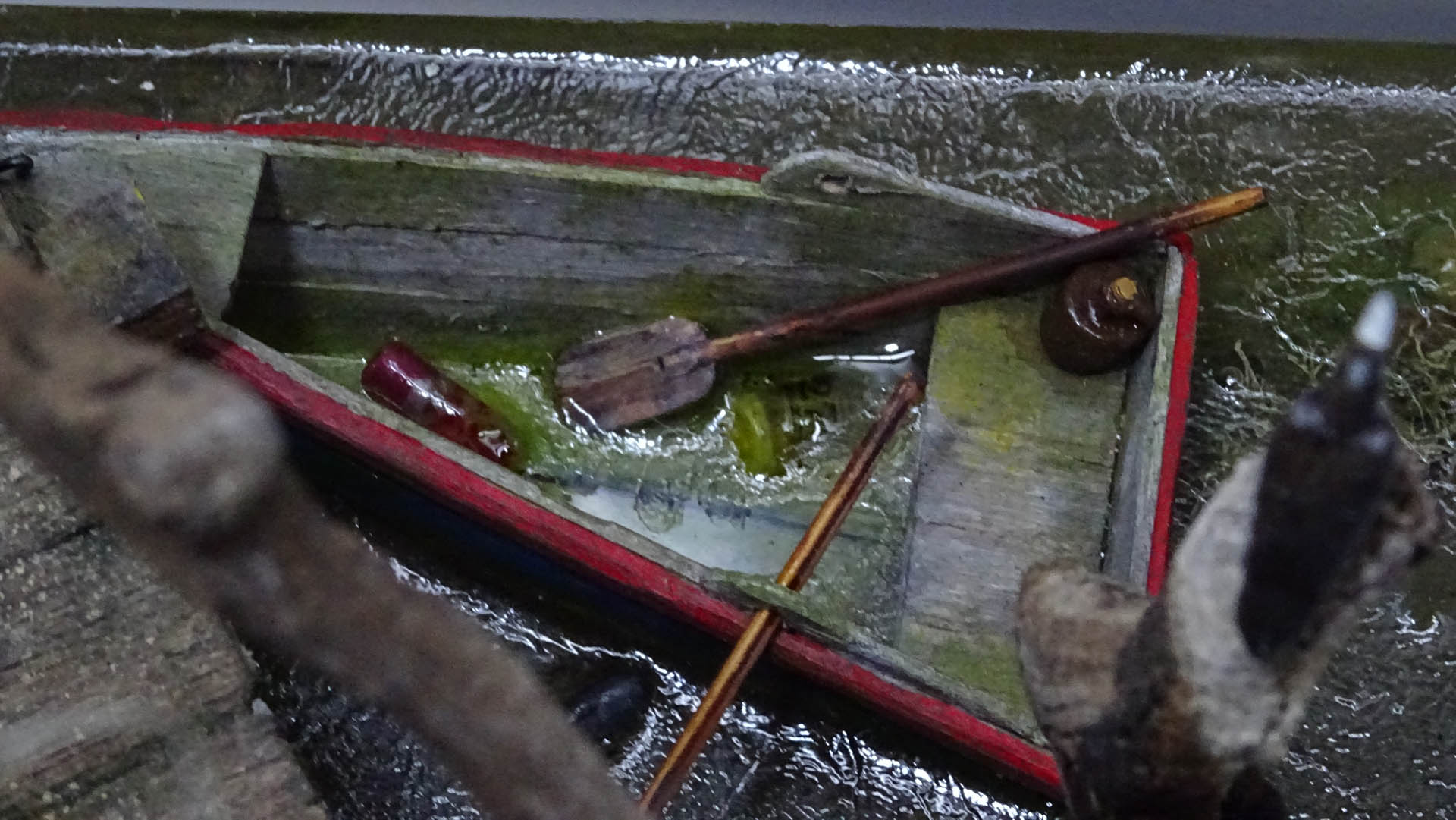 Diorama artístico de una cabaña de madera azul envejecida sobre pilotes en un pantano, con efectos de agua estancada, un bote de remos y detalles de vegetación pantanosa.