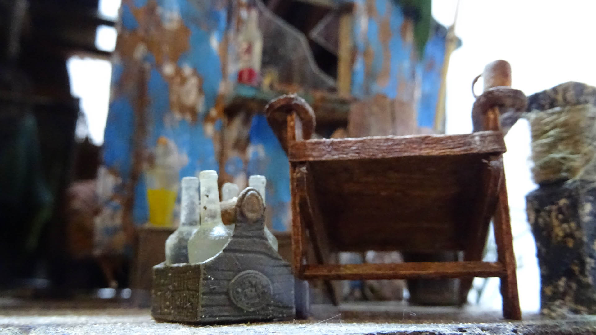Diorama artístico de una cabaña de madera azul envejecida sobre pilotes en un pantano, con efectos de agua estancada, un bote de remos y detalles de vegetación pantanosa.