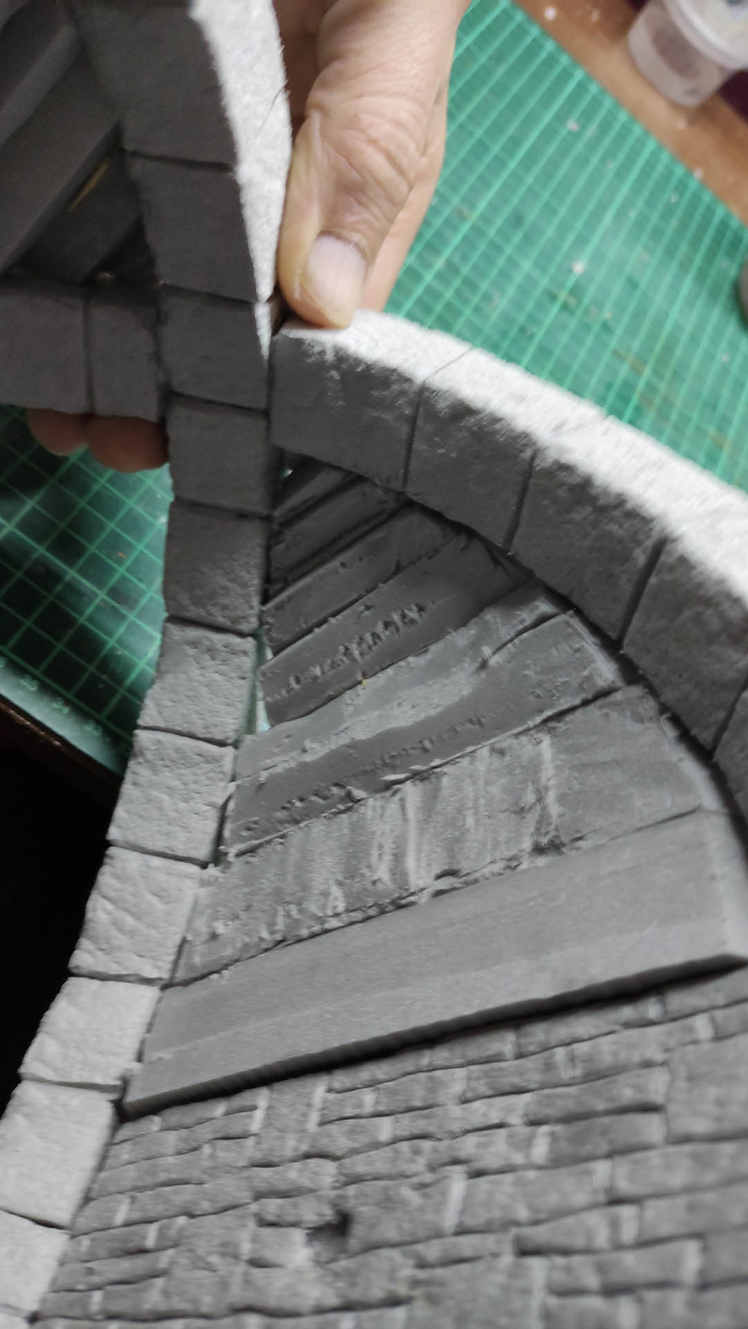 Diorama artesanal detallado de un duende y un pozo estructurado en tres niveles. El nivel superior recrea un jardín exterior exuberante utilizando vegetación natural y preservada (musgos y enredaderas), sobre estancias subterráneas de piedra y madera