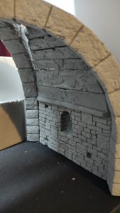 Diorama artesanal detallado de un duende y un pozo estructurado en tres niveles. El nivel superior recrea un jardín exterior exuberante utilizando vegetación natural y preservada (musgos y enredaderas), sobre estancias subterráneas de piedra y madera