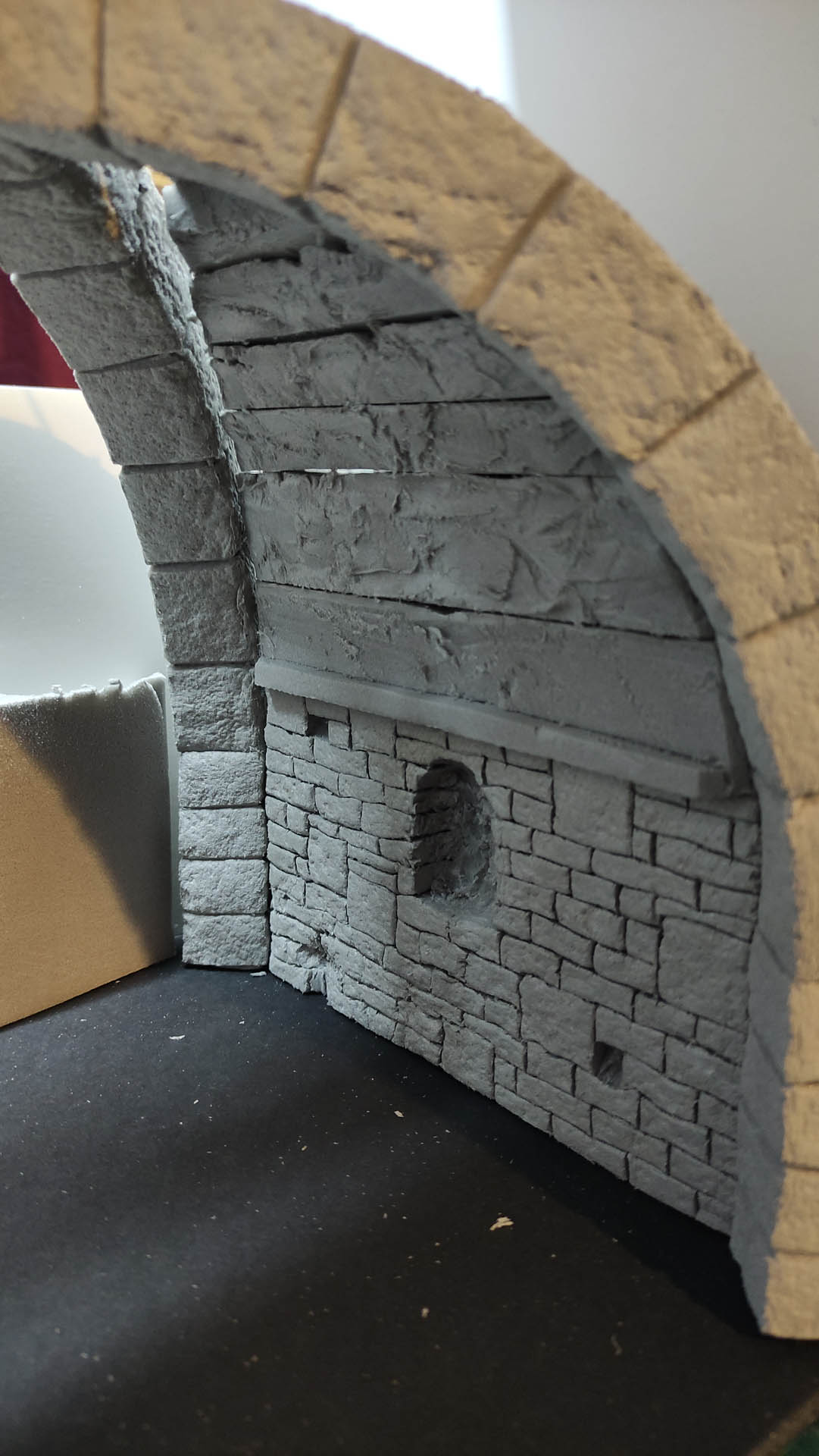 Diorama artesanal detallado de un duende y un pozo estructurado en tres niveles. El nivel superior recrea un jardín exterior exuberante utilizando vegetación natural y preservada (musgos y enredaderas), sobre estancias subterráneas de piedra y madera