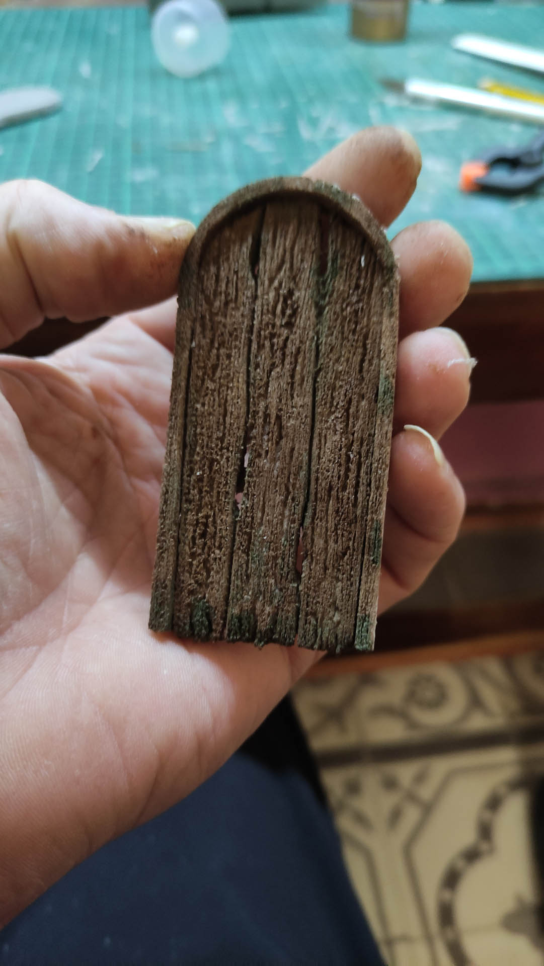 Diorama artesanal detallado de un duende y un pozo estructurado en tres niveles. El nivel superior recrea un jardín exterior exuberante utilizando vegetación natural y preservada (musgos y enredaderas), sobre estancias subterráneas de piedra y madera